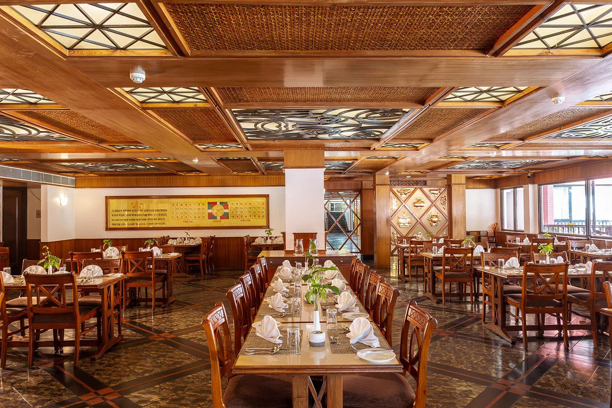 Dining room with wooden tables and a carved ceiling at Pokhara Grande