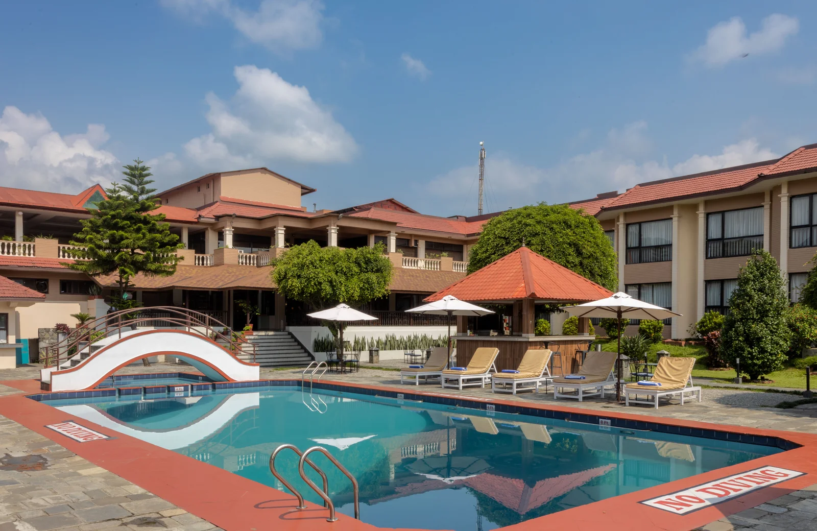 Outdoor swimming pool, bridge and loungers at Pokhara Grande